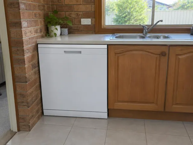 White dishwasher fitted under a kitchen bench beside timber cabinets and a stainless sink in Belmont