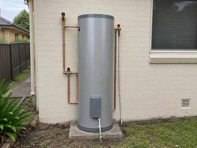 Outdoor hot water cylinder on a concrete pad beside a cream brick house in Belmont South