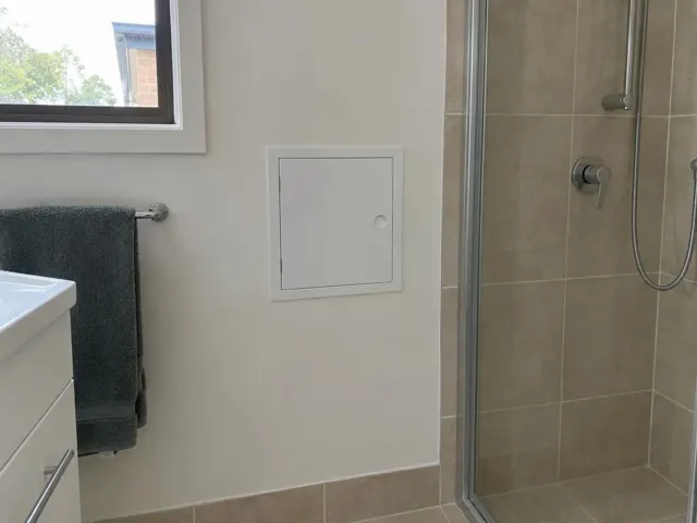 Bathroom wall with a neat access panel beside a tiled shower in Belmont