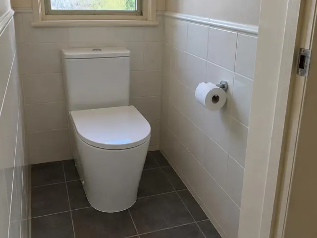 White toilet in a small tiled bathroom with a window and toilet roll holder in Redhead